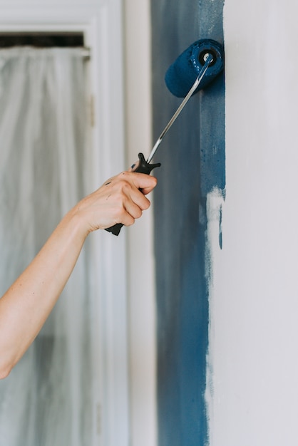 A woman applying blue paint to a wall, representing painting services for residential and commercial properties.