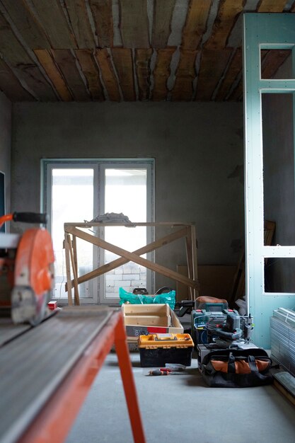 A cluttered room featuring various tools and wooden materials scattered across the floor, suggesting a home improvement project.